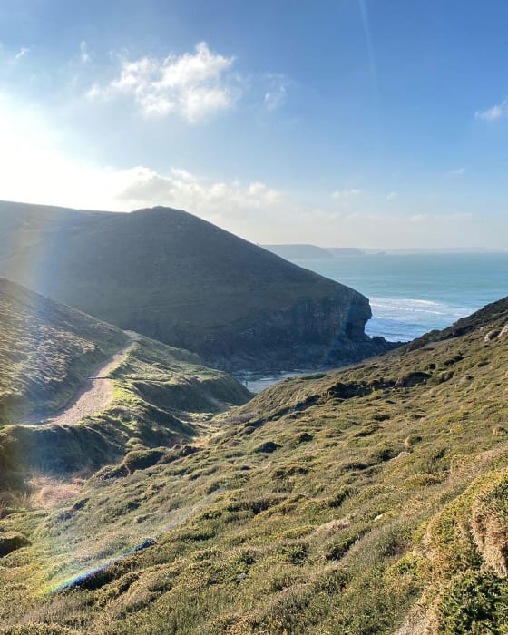 A view over the grassy cliffs down to a small cove Chapel Porth Beach in Cornwall