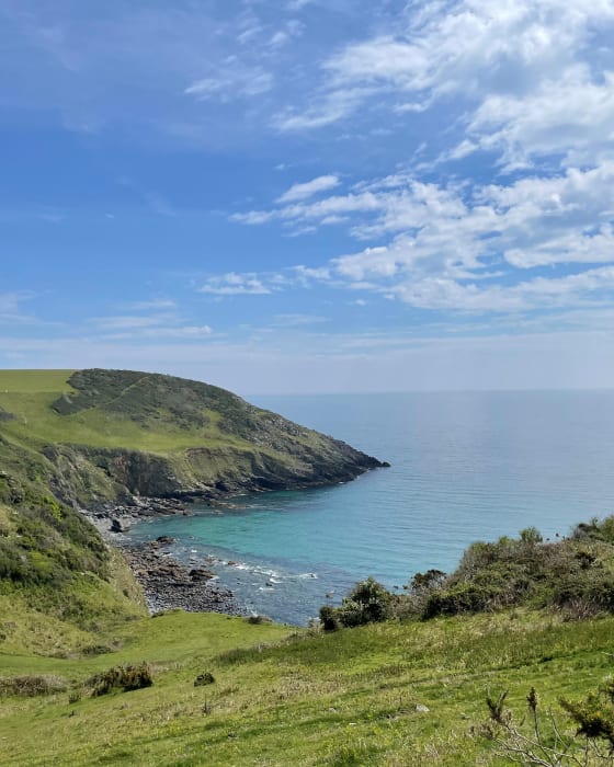 A view of grassy cliffs and a clear blue sea The Cornish Coast on a sunny day