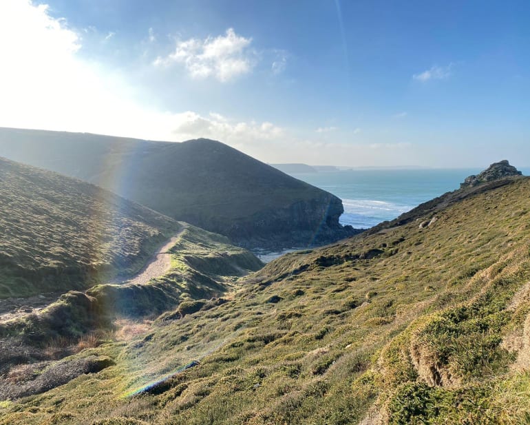 A view over the grassy cliffs down to a small cove Chapel Porth Beach in Cornwall