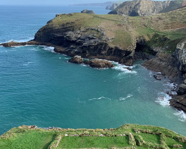 A winding sandy path under a green bush that has grown into an archway The coast path near Polperro